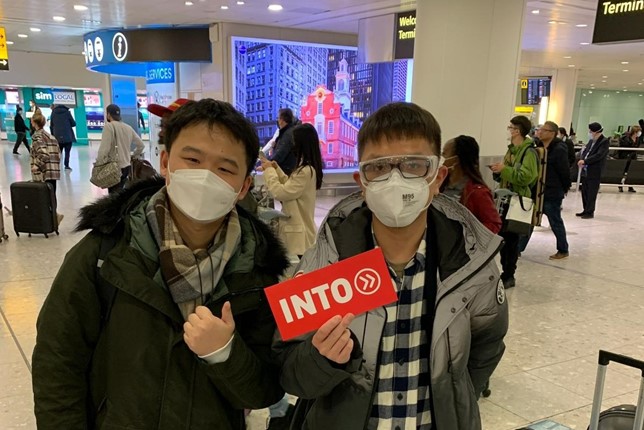Two INTO Chinese students wearing face masks pose with INTO ticketholder at London Heathrow airport after charter flight from Shanghai.